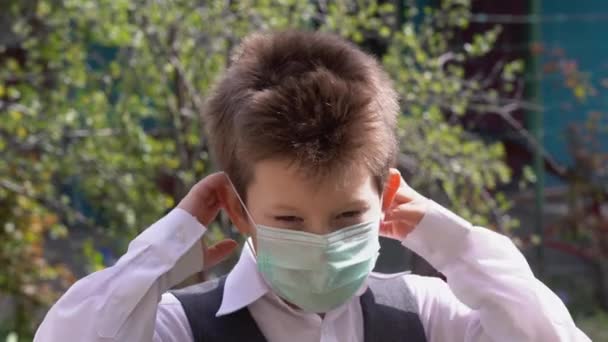 美しい白人の生徒ブロンドの子供は 緑の日当たりの良い庭の屋外の閉鎖を背景に ウイルスからターコイズ保護医療用マスクを着用しています Covid 19コロナウイルス保護コンセプト — ストック動画