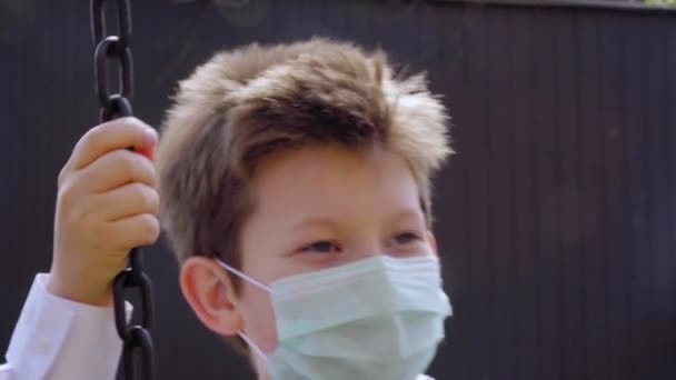 셔츠를 금발의 아이가 마스크를 그네를 녹슬어 체인을 배경에 미소를 짓는다 — 비디오
