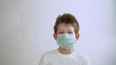 Gri kollu, uzun kollu, maske takan mutlu, yakışıklı çocuk gülümseyecek ve beyaz arka planda zevkle maskesini çıkaracak. Küçük çocuk karantina ve tecrit dönemine rağmen hayatın tadını çıkarıyor..