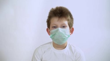 Koruyucu turkuaz maskeli uzun kollu sarışın çocuk gri arka planda bir inkar hareketi ya da olumsuzluk yapıyor. Erkek, başını soldan sağa sallıyor. Söyleme..