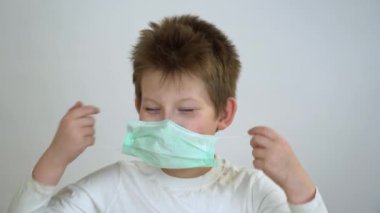 Beyaz tişörtlü sevimli genç adam gülüyor, gülümsüyor ve gri arka planda koruyucu tıbbi maske takıyor. Çocuk Corona virüsünden ve grip salgınından korkmuyor. Covid 19 virüs koruma kavramı. 