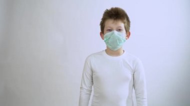 Mavi koruyucu maskeli, kısa sarı saçlı küçük çocuk neşelen, dans et, yakından gülümse. Mutlu çocuk yüz solunum cihazı takıyor ve Corona virüsü ve grip salgını sırasında hayatın tadını çıkarıyor. İyileşme konsepti.