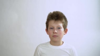 Beyaz tişörtlü, mavi gözlü yakışıklı, ciddi sarışın genç adam koruyucu bir tıbbi maske takıyor. Kameraya bakan çocuğun portresi. Gri arkaplanda izole.