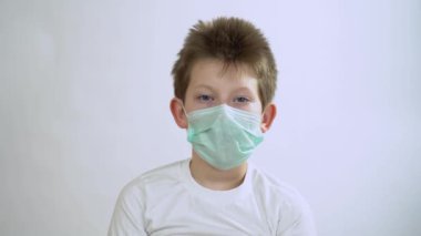 Suratı koruyucu maske takan mavi gözlü, beyaz saçlı yakışıklı beyaz adam beyaz duvarda gözlerini açıyor. Corona virüsünden korkan sevimli bir çocuğun portresi. Korkuyu hisseder.