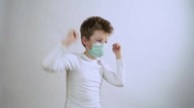 Beyaz uzun kollu koruyucu tıbbi maskeli genç sarışın adam mutlu, dans ediyor, gri duvarda gülümsüyor yakın plan. Mutlu çocuk Coronavirus ve grip salgını sırasında hayatın tadını çıkarıyor. İyileşme konsepti.