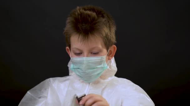 害怕英俊的金发碧眼的小男孩 穿着白色的防护服 戴着两个蓝色的面具和一个呼吸口罩 面对着黑色的背景 Covid 19病毒保护概念 — 图库视频影像