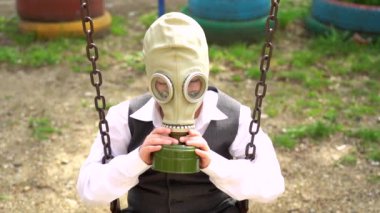 Çocuk metal paslı zincirlerle salıncakta oturuyor, yüzüne koruyucu ordu gaz maskesi takıyor, kameraya bak. Yalnız adam Corona virüsü enfeksiyonundan dolayı solunum cihazı takıyor ve üzgün..