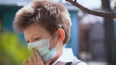Koruyucu tıbbi maske takan küçük üzgün çocuk elleriyle ağzını tutuyor, yüzünü kapatıyor, aşağıya bakıyor, dışarıda ağır çekimde nefes almak zor. Korkan adam korkunç trajedileri ve ölü insanları hatırlar.