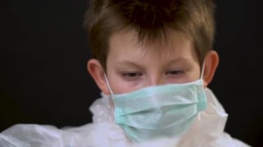 Mavi eldivenli beyaz koruyucu giysili güzel sarışın çocuk maske takmış, yüzüne solunum cihazı takmış, siyah arka plana kaput takmış. Koronavirüs konsepti nedeniyle karantina.