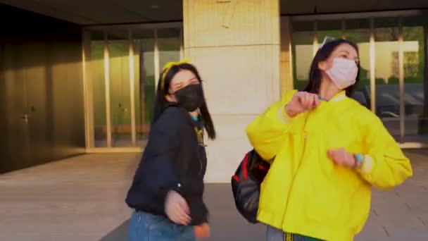 Två Glada Flickor Jackor Dansar Glatt Medicinska Skyddande Ansiktsmasker Bakgrunden — Stockvideo