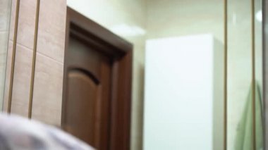 Güzel esmer, genç bir kız yeşil bir havluyla yüzünü siliyor koruyucu bir tıbbi maske takıyor ve sabahları banyoda aynanın önünde cildine bakıyor. Corona virüsü tehdidiyle karantina.