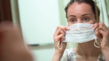 Güzel bir Rus esmer kız aynaya bakar ve sabahları banyoda mavi koruyucu bir maske takar. Günün başlangıcında kovid19 virüs izolasyon süresi. 