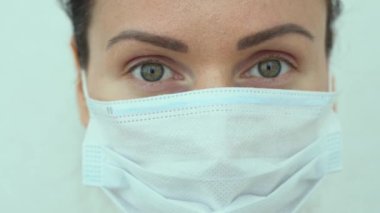 Rus hemşirenin güzel yeşil gözleri, beyaz arka planda izole edilmiş göz kırpmaları. Mavi koruyucu tıbbi maske takan beyaz bir kadının portresi. Salgın sırasında karantina.