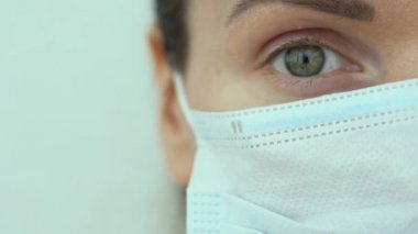 Rus doktorun tek harika yeşil gözü beyaz arka planda izole bir şekilde ileriye bakıyor. Mavi koruyucu tıbbi maske takan beyaz bir kadının portresi. Coronavirus covid-19 virüs tehdidi.