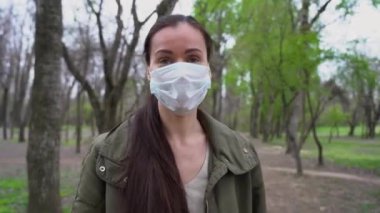 Medikal maskeli, uzun kahverengi saçlı çekici beyaz kadın kameraya, ağaçlar arasında bir parmakla orman yolunu işaret ederek nereye gidileceğini gösteriyor. Tecrit süresi.