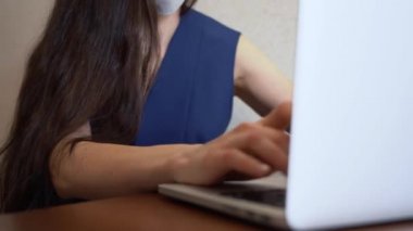 Mavi ofis elbiseli, uzun kahverengi saçlı, beyaz iş kadını yüz maskesi takıyor, dizüstü bilgisayar kullanıyor, evdeki çalışanlara e-posta yazıyor. Kız bilgisayarda çalışıyor. Covid-19 virüsünden izolasyon.