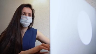 Laptop kullanan, medikal maskeli esmer iş kadını. Güzel kız mesajlar, okumalar, cevap e-postaları, sörf siteleri. Salgın karantina günlerinde evde bilgisayarla çalışan bekar bir kadın..