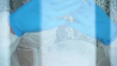 Beyaz koruyucu takım elbiseli, yüz maskeli, camdan dışarı bakan, el ve alnını cama dayayıp sarılan üzgün kızın portresini yakından çek. Coronavirus tarafından karantina altına alınmış bir kadın..