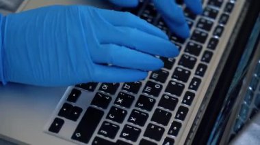 Yakından tanınmayan bir adam internette dezenfekte edilmiş mavi eldivenlerle dizüstü bilgisayarda çalışıyor. Kadın elleri klavyede yazı yazıyor. Başarılı iş kadını internette sörf yapıyor. Yakın çekim..