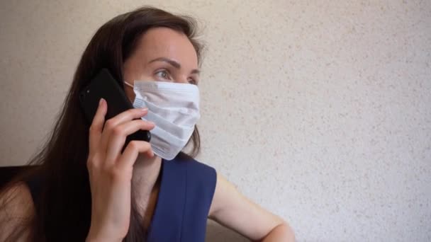 年轻的黑发女企业家身穿防护性医疗面罩 用手机 在家远程工作 在被Covid 19威胁隔离期间 生病的女经理用手机交谈 — 图库视频影像