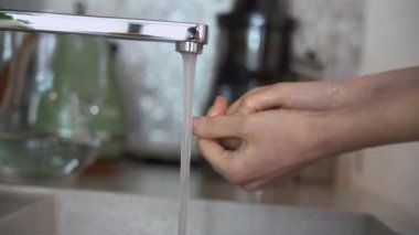 Metal musluktan ya da musluktan gelen saf sıcak suya kadın ellerini kapat, parmaklarını sık sık ovuştur, su evdeki lavaboda ellerinden akar. Koronavirüs salgını önleme