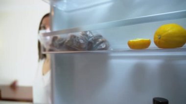 Koruyucu tıbbi maskeli, beyaz tişörtlü güzel esmer kadın buzdolabından büyük, lezzetli bir portakal alır. İçeriden. Kız tecritte kalsın. Kendini karantina altına al. COVID-19..