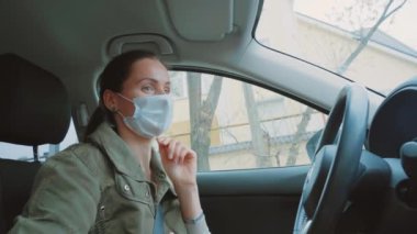 Yeşil kışlık ceketli harika Kafkasyalı genç esmer kız güneşli bir günde mavi koruma maskesi takıyor. Kahverengi at kuyruğu saçlı mutlu kadın arabanın içinde dans ediyor. İç görünüm. 
