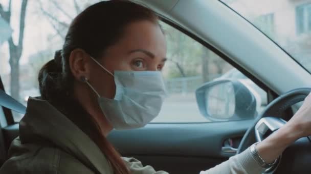 漂亮的白人女孩戴着蓝色防护医疗面罩 手持黑色方向盘 司机环顾四周 检查是否有其他车辆 布鲁内特的女人左右转弯 — 图库视频影像