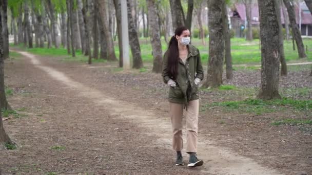 長い茶色の髪を持つ保護医療面マスクで素晴らしいかわいいロシアの女性は夏の森の中で一人で歩き 自然と新鮮な空気を楽しんで 空の屋外で太陽を見上げています 隔離概念 — ストック動画
