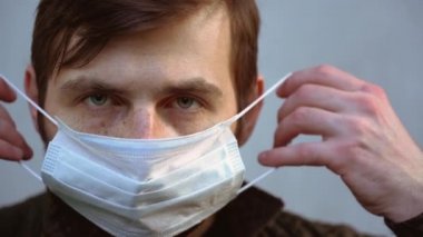 Kahverengi saçlı, beyaz sakallı güzel iş adamı koruyucu tıbbi maske takıyor. Adam arka plandaki gri duvara yakından bakıyor. Coronavirus covid-19 virüsü ile karantina 