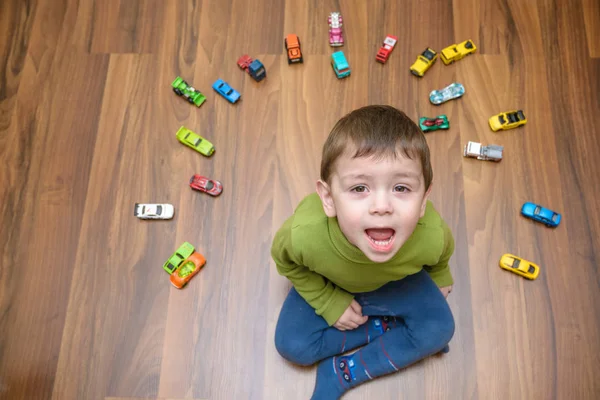 室内のおもちゃの車がたくさん遊んで少し白人の子。緑のシャツを着ている少年を子供します。家庭で楽しんで幸せな幼稚園や保育園 — ストック写真