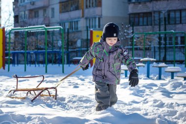 Açık havada kış şehirde yürüyüş çocuk mutlu onun kızak sürükler. Çocuk gülen ve having fun.