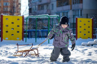 Açık havada kış şehirde yürüyüş çocuk mutlu onun kızak sürükler. Çocuk gülen ve having fun.