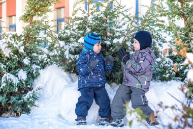 İki küçük çocuklar renkli giysiler açık havada kar yağışı sırasında oynayan çocuk. Kışın soğuk günlerinde çocuklu etkin boş. Mutlu kardeşler ve eğleniyor İkizler kar