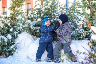 İki küçük çocuklar renkli giysiler açık havada kar yağışı sırasında oynayan çocuk. Kışın soğuk günlerinde çocuklu etkin boş. Mutlu kardeşler ve eğleniyor İkizler kar