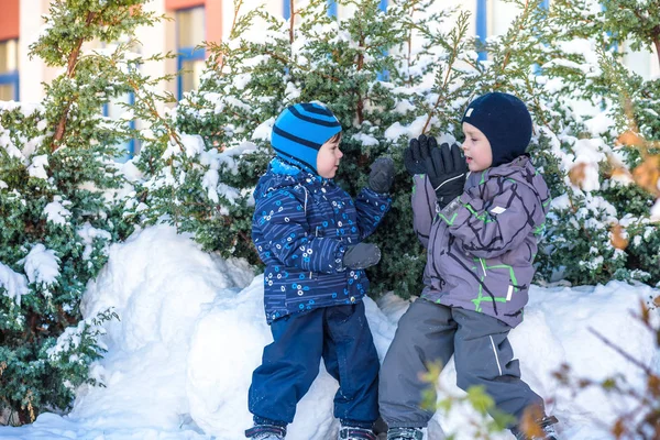 Due ragazzini in abiti colorati che giocano all'aperto durante le nevicate. Tempo libero attivo con i bambini in inverno nelle giornate fredde. Buoni fratelli e gemelli che si divertono con la neve — Foto Stock