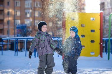 İki küçük çocuklar renkli giysiler açık havada kar yağışı sırasında oynayan çocuk. Kışın soğuk günlerinde çocuklu etkin boş. Mutlu kardeşler ve eğleniyor İkizler kar