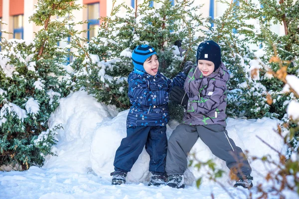 İki küçük çocuklar renkli giysiler açık havada kar yağışı sırasında oynayan çocuk. Kışın soğuk günlerinde çocuklu etkin boş. Mutlu kardeşler ve eğleniyor İkizler kar
