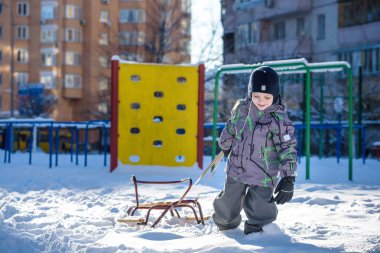 Açık havada kış şehirde yürüyüş çocuk mutlu onun kızak sürükler. Çocuk gülen ve having fun.