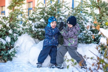 İki küçük çocuklar renkli giysiler açık havada kar yağışı sırasında oynayan çocuk. Kışın soğuk günlerinde çocuklu etkin boş. Mutlu kardeşler ve eğleniyor İkizler kar