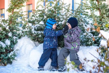 İki küçük çocuklar renkli giysiler açık havada kar yağışı sırasında oynayan çocuk. Kışın soğuk günlerinde çocuklu etkin boş. Mutlu kardeşler ve eğleniyor İkizler kar