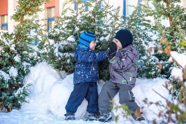 İki küçük çocuklar renkli giysiler açık havada kar yağışı sırasında oynayan çocuk. Kışın soğuk günlerinde çocuklu etkin boş. Mutlu kardeşler ve eğleniyor İkizler kar