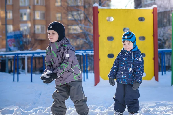 Two little kid boys in colorful clothes playing outdoors during snowfall. Active leisure with children in winter on cold days. Happy siblings and twins having fun snow — Stock Photo, Image