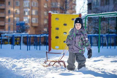Açık havada kış şehirde yürüyüş çocuk mutlu onun kızak sürükler. Çocuk gülen ve having fun.