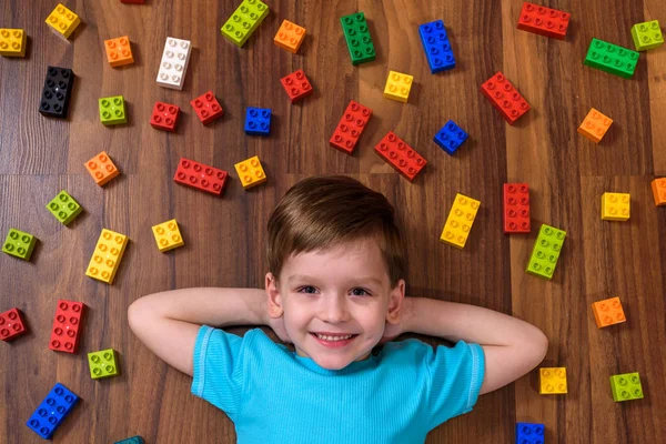 Pequeño niño caucásico jugando con un montón de bloques de plástico de colores en el interior. Niño niño vistiendo camisa y divertirse creando — Foto de Stock
