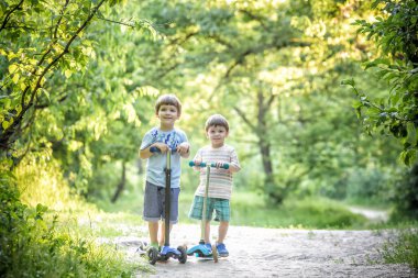 İki sevimli çocuklar, rekabet scooter, park, açık sürme yaz.