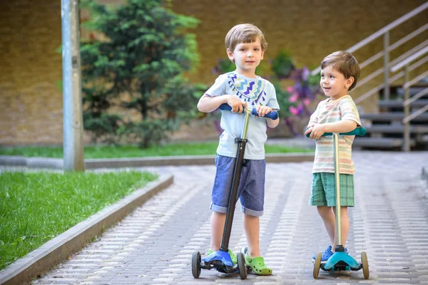 Dos chicos lindos, competir en scooters a caballo, al aire libre en el parque, verano . —  Fotos de Stock