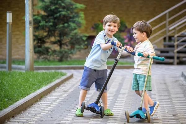 Dois meninos bonitos, competir em scooters de equitação, ao ar livre no parque , — Fotografia de Stock