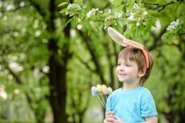 Küçük çocuk bahar bahçesinde paskalya yumurtası arıyor. Şirin. 