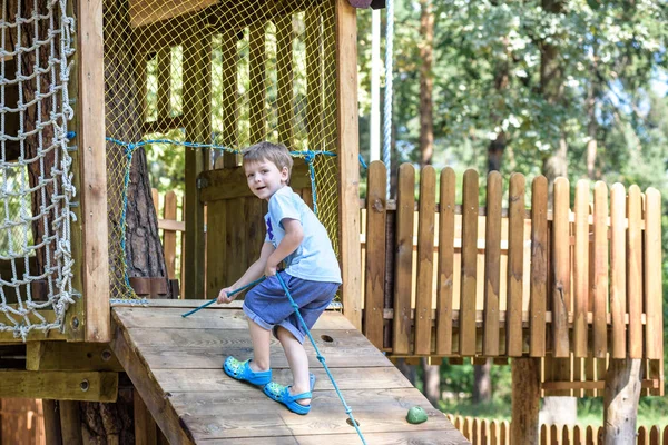 Little climber takes the rope bridge. Boy has fun time, kid climbing on sunny warm summer day — Stock Photo, Image